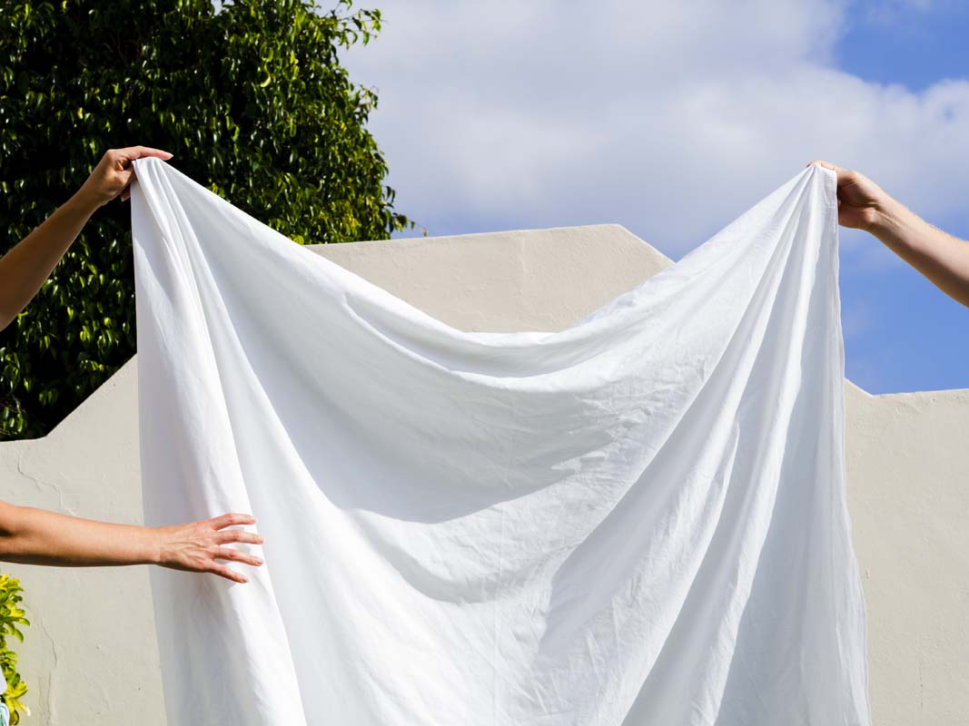 Freshly washed white bed sheets on a made bed